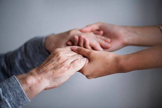 Zwei jüngere Hände halten behutsam die Hand eines älteren Menschen.